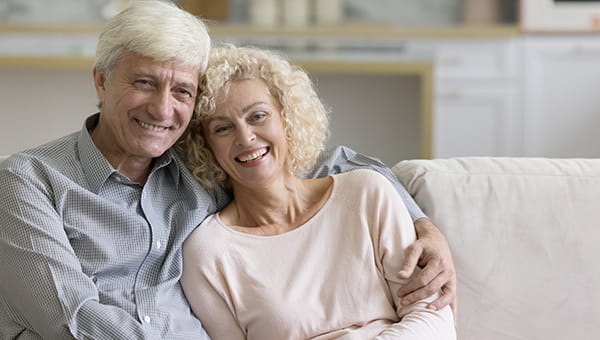 An elderly man and woman sitting on the couch with the man having his arm around the woman