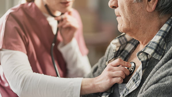 A nurse putting a stethoscope on a patient's chest checking for heart rhythm