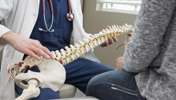 A doctor holding a 3D model of a spine and discussing with a patient.