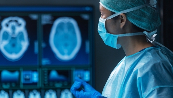 A medical professional scrubbed into a surgical setting, analyzing a brain scan.