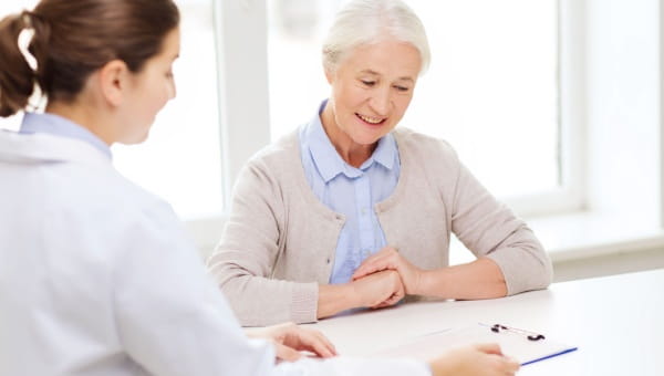 A woman smiles while talking with a physician at a table with a clipboard on it.