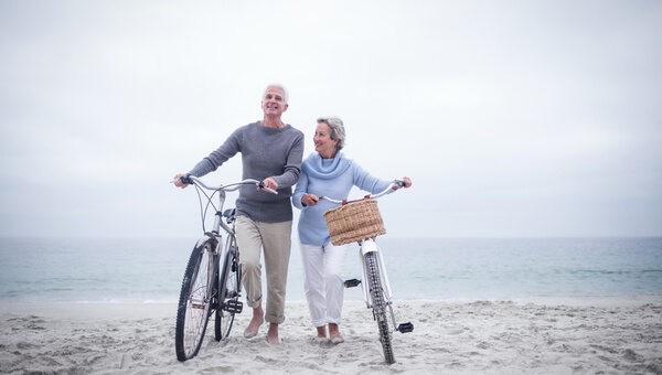 A senior couple is walking with their bicycles at the beach.