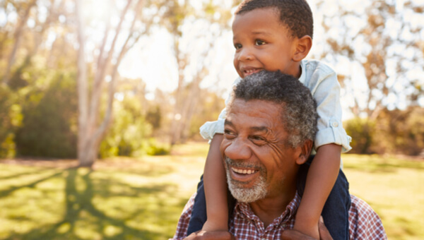 A grandfather is carrying his grandson on his shoulders.