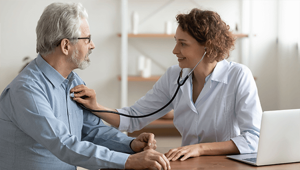 a physician holding her stethoscope to an older male patient