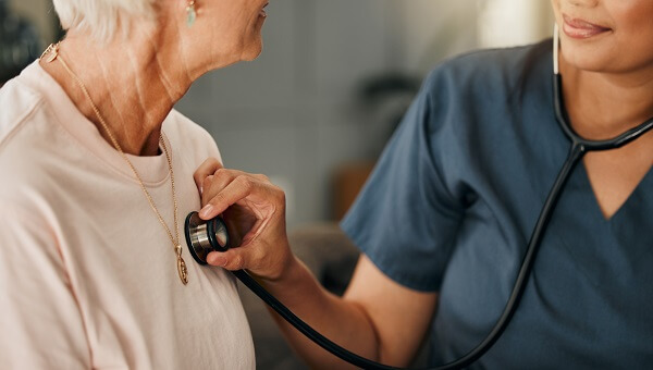 female doctor holding stethoscope to elderly womans chest