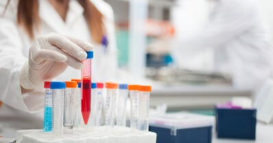 A woman in a lab coat with protective gloves works with glass vials