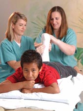Young boy lying on a table while two nurses wrap a broken leg bone