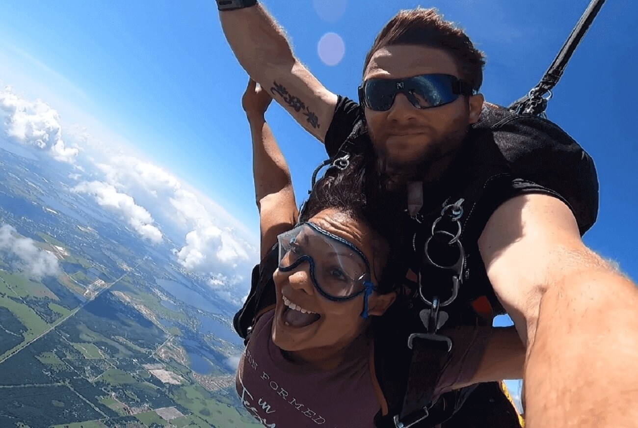 excited woman and man skydiving with landscape and clouds in the background