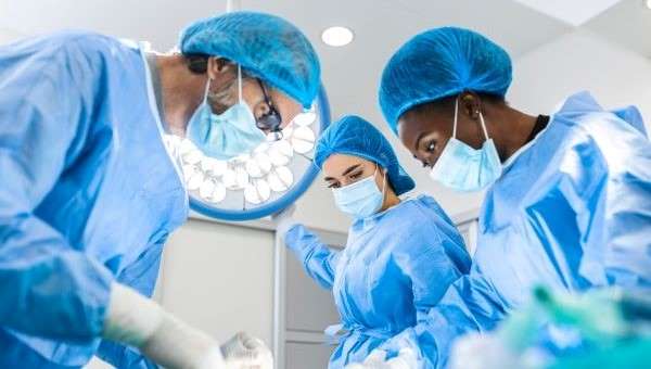 three surgeons wearing gowns caps and gloves performing an operation