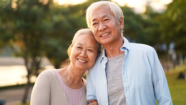 A senior couple is smiling and walking together in a park.