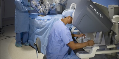 A surgeon looking into an apparatus and moving the hands of a robotic surgeon
