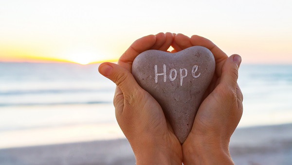 A person is holding a heart-shaped stone with the word "Hope" on it.