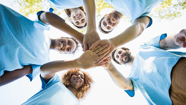 A group of men and women are standing in a circle and have extended their right arms so they can place their right hands on top of each other.