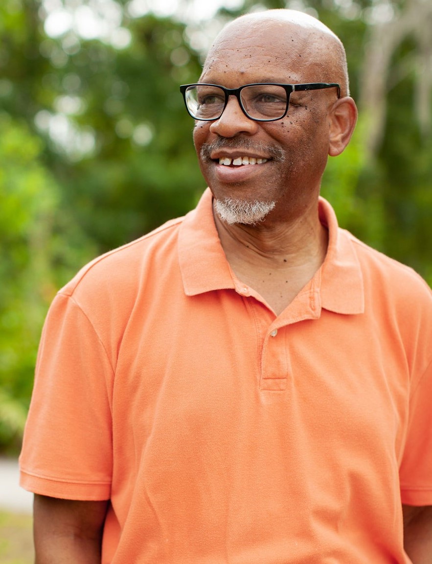 Senior black man smiling with glasses and an orange collared shirt on