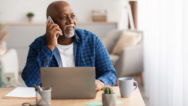 African American man sitting at a table in front of a laptop talking on his cell phone