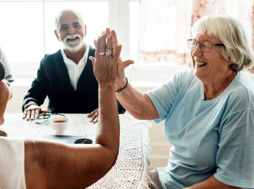 A group of people sitting at a table smiling with a lady high fiving another lady.