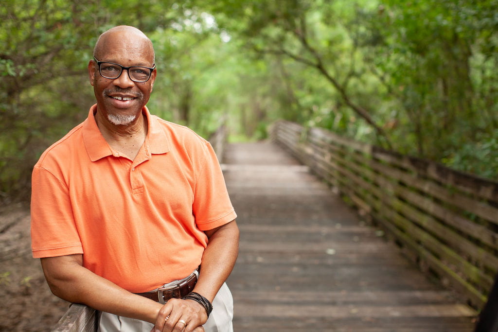 Man standing on a wooden bridge under a canopy of trees