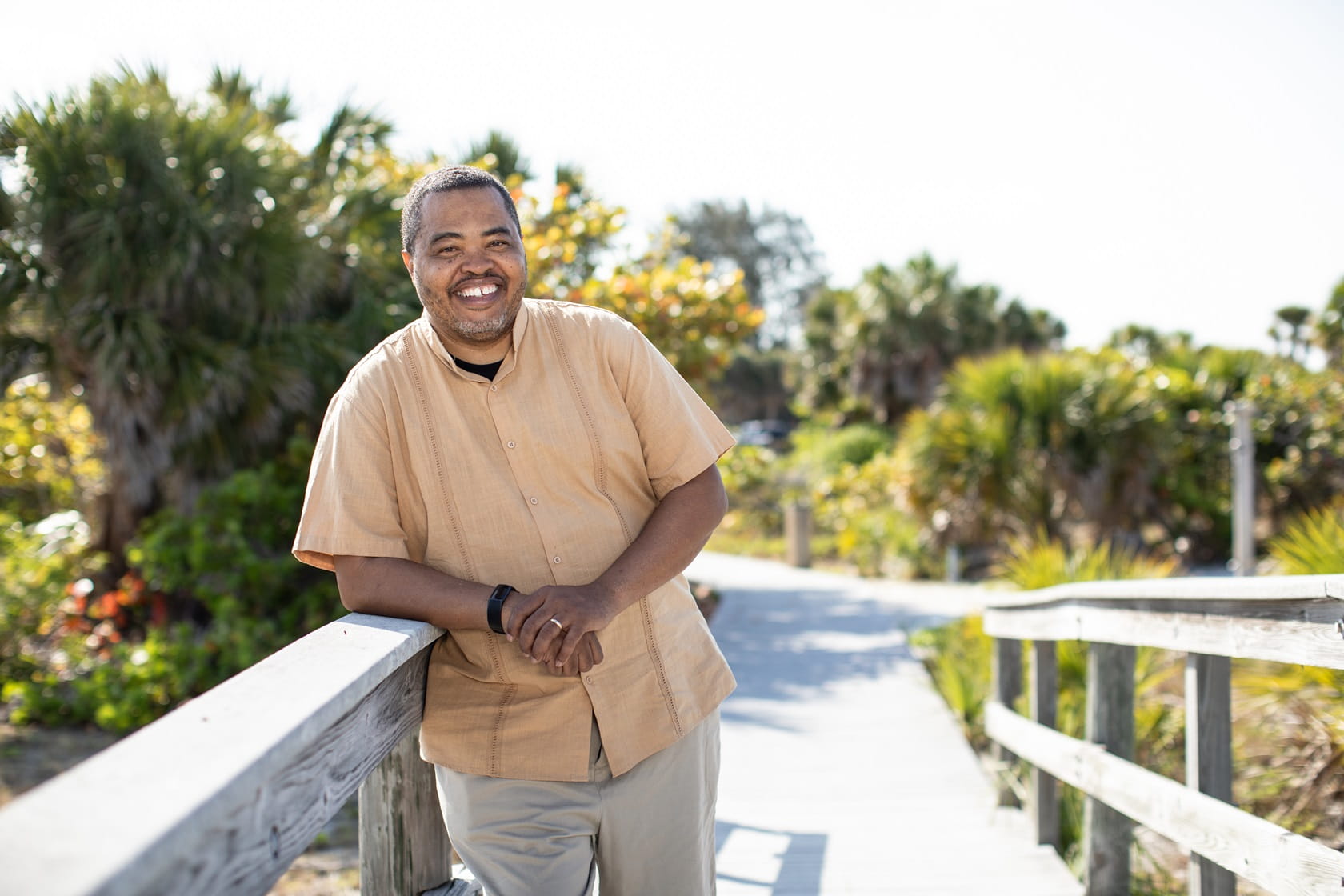 person standing on a boardwalk with palm trees and lush landscaping in the background