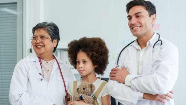 A group of providers standing in support of a young patient holding a teddy bear