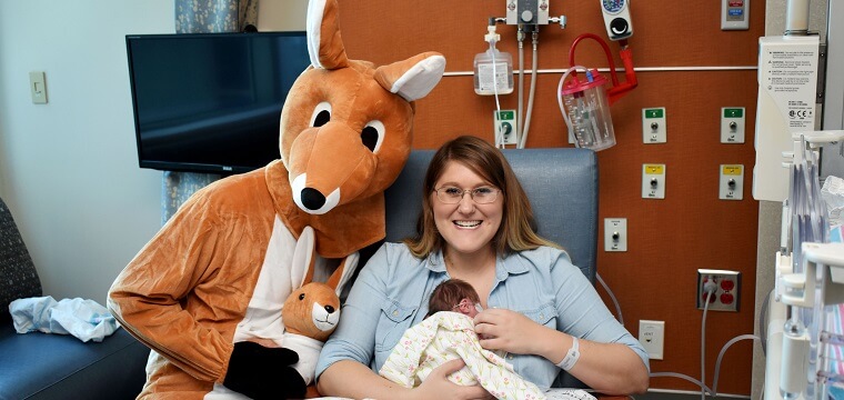 A mom using kangaroo care with an infant while a person in a kangaroo costume is next to them