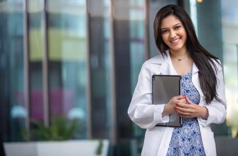 Happy smiling young Indian American professional in the medical field, possibly dental, therapy, medicine, doctor, with computer