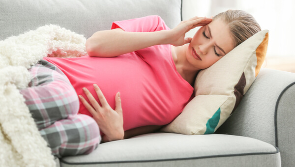 pregnant woman holding head and stomach while laying down