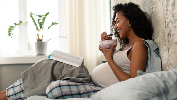 pregnant woman sitting on couch eating food and smiling