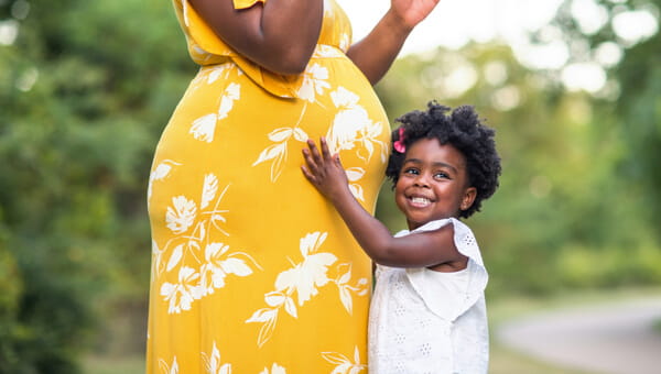 young smiling girl holding on to her pregnant mother
