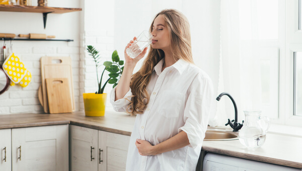 pregnant woman in her kitchen drinking water