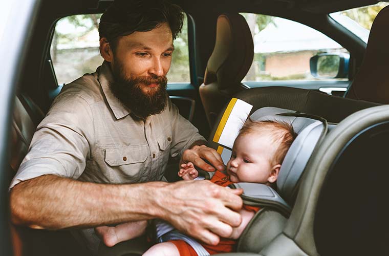 Dad buckling baby in car seat.