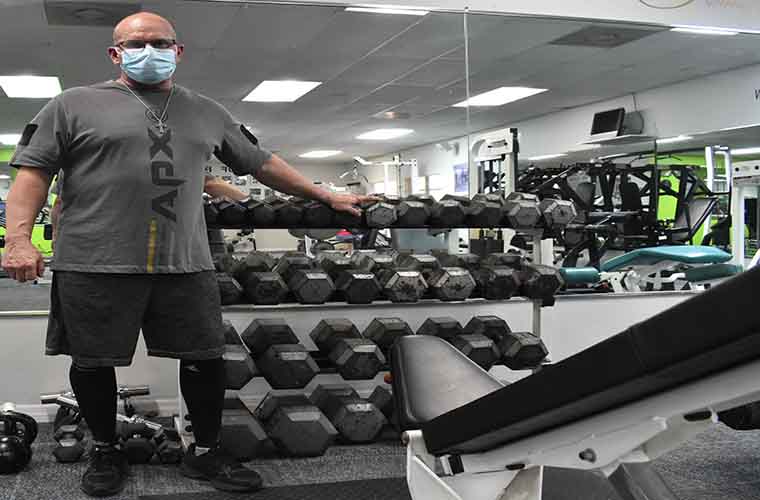 Mark Metzger in his Tampa gym in front of a dumbbell rack