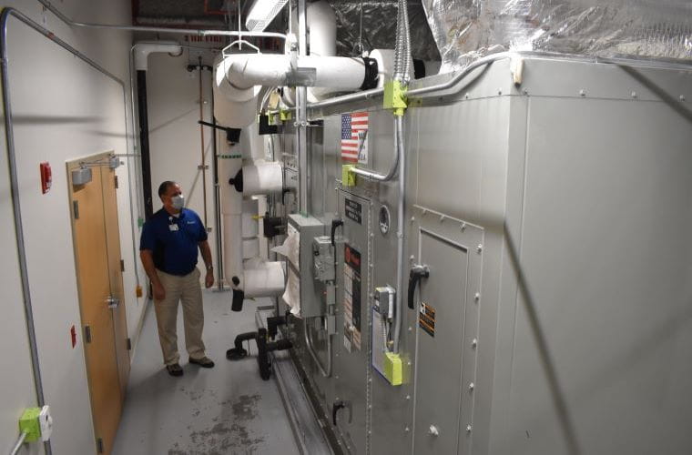 John in front of an air handler which moves air conditioning into an occupied space.