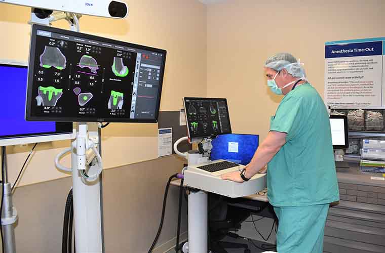 In a simulation, Dr. Grayson pre-plans the knee replacement surgery in 3-D. He is in a surgical suite looking at a monitor of knee images.