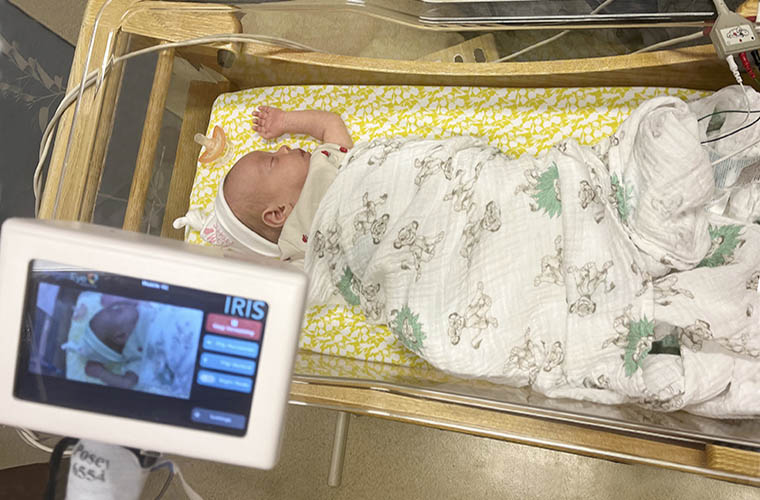 A small camera screen looks over a newborn baby in a NICU bed.
