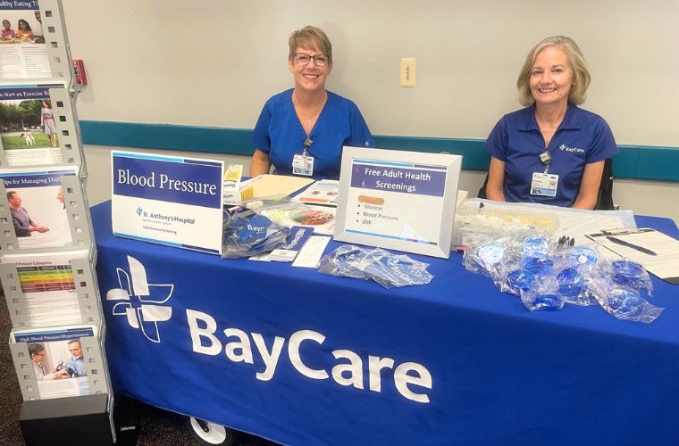 Two women are sitting at a table with a blue BayCare tablecloth with health materials and information in front of them.