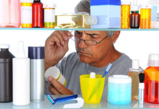 Middle aged man reading a prescription label in front of his bathroom medicine cabinet.