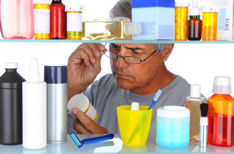 Middle aged man reading a prescription label in front of his bathroom medicine cabinet.