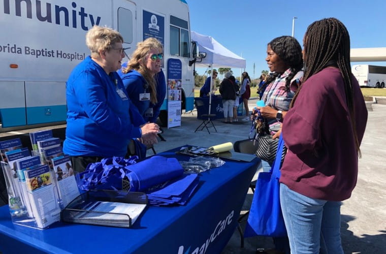 BayCare Team Members in blue shirts, talk with two members of the community outside at vendor table.