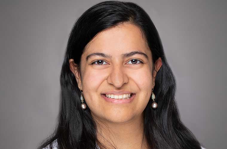 A woman with long dark hair and two-tiered earrings smiles for the camera.