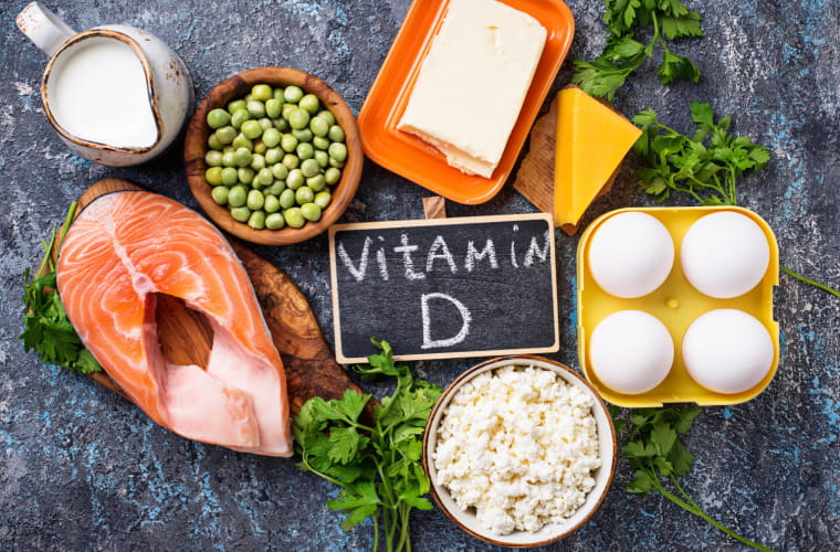 Assortment of high vitamin D sources like milk, salmon, cheese and eggs circle a sign in the middle that says vitamin D.