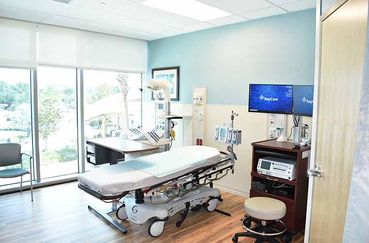 A new assessment room includes monitors, a hospital bed and an infant warmer. A large window shows trees and the entrance to the hospital.