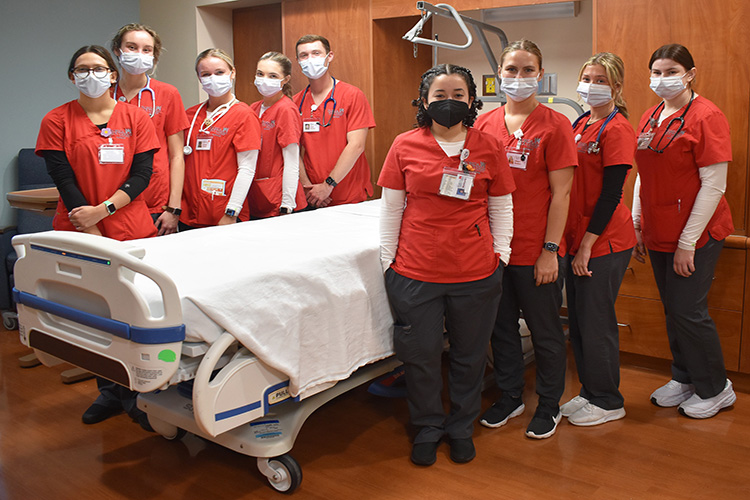 Group of nursing students posing around a stretcher in a hospital room.