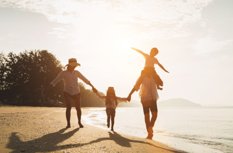 Father, mother and their two children are playing together on a tropical beach with the sunset in the background.