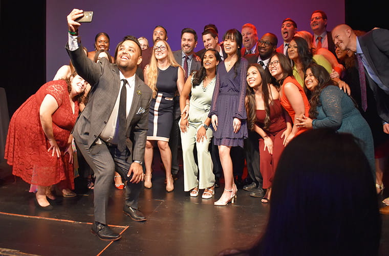 Man takes selfie photo with group of people behind him at graduation ceremony.