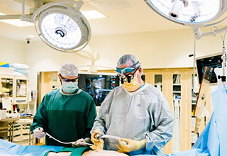 Two surgeons in an operating room standing over the operating table preparing to perform surgery.