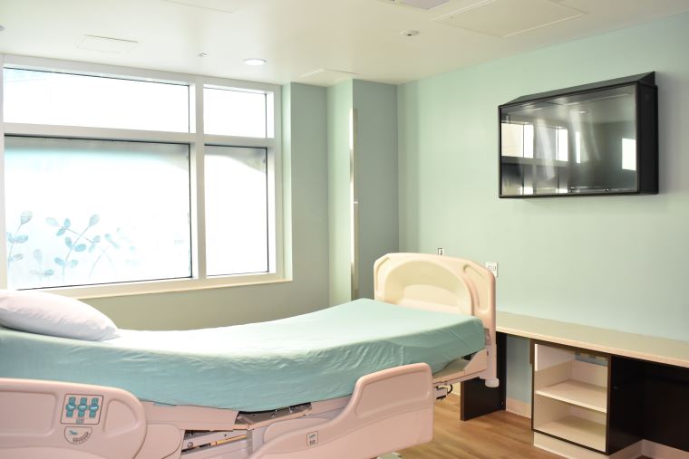 A patient room with a plexiglass safety feature over a television attached to the wall