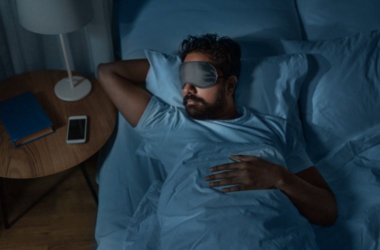 Man sleeps comfortably in bed wearing eye mask.