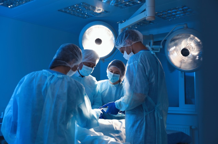 Clinicians in blue scrubs work carefully in an operating room.
