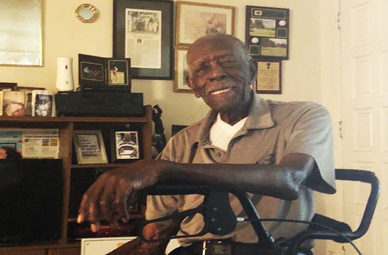 Man sits in his living room with plaques and awards in the background. 