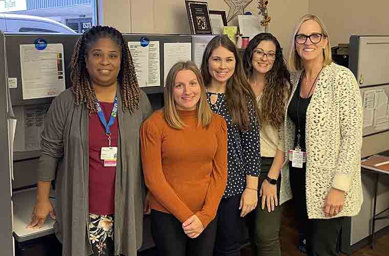 Five women standing in front of a desk smiling at the camera.